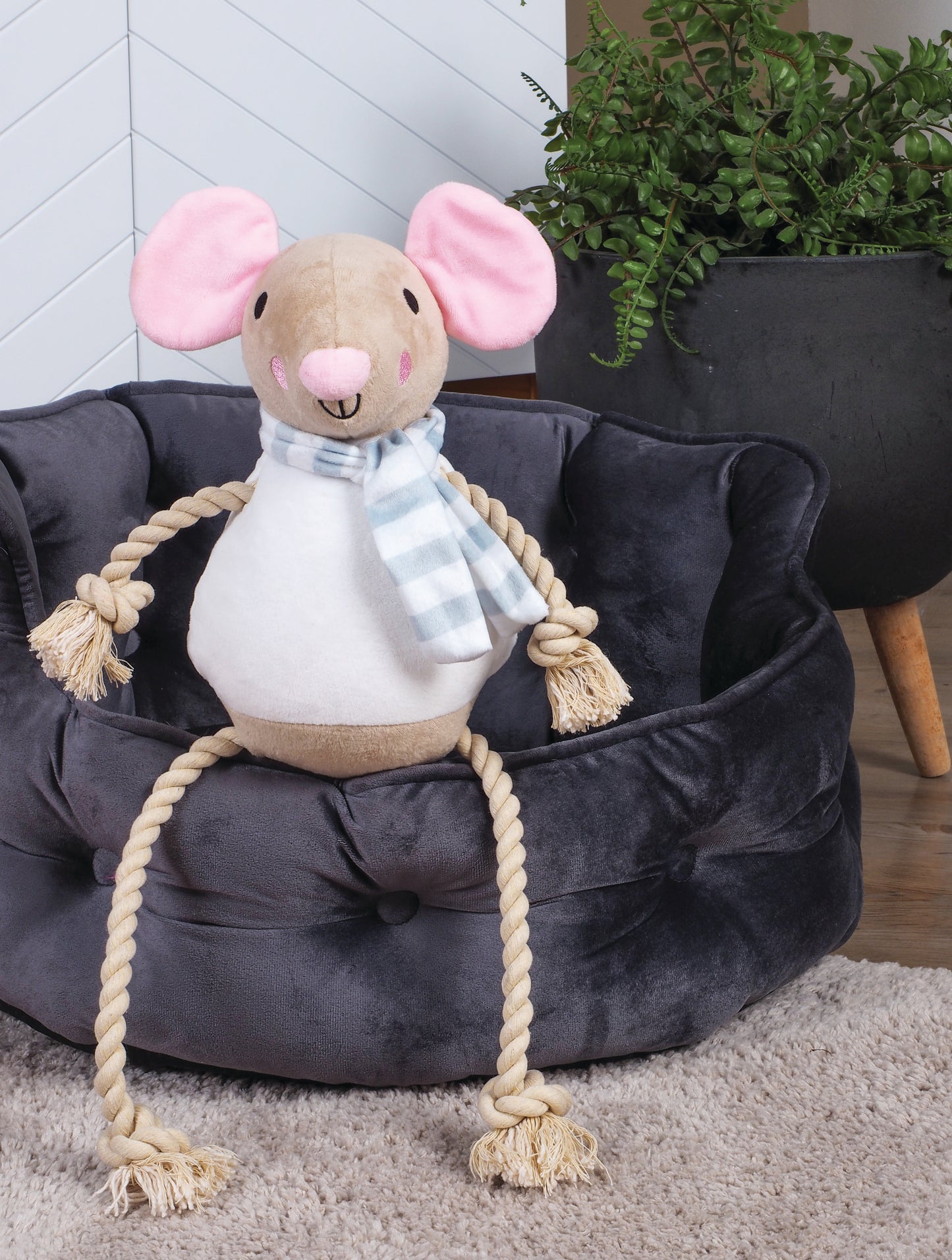 Plush mouse toy with a rope on a navy blue pet bed in a room setting.