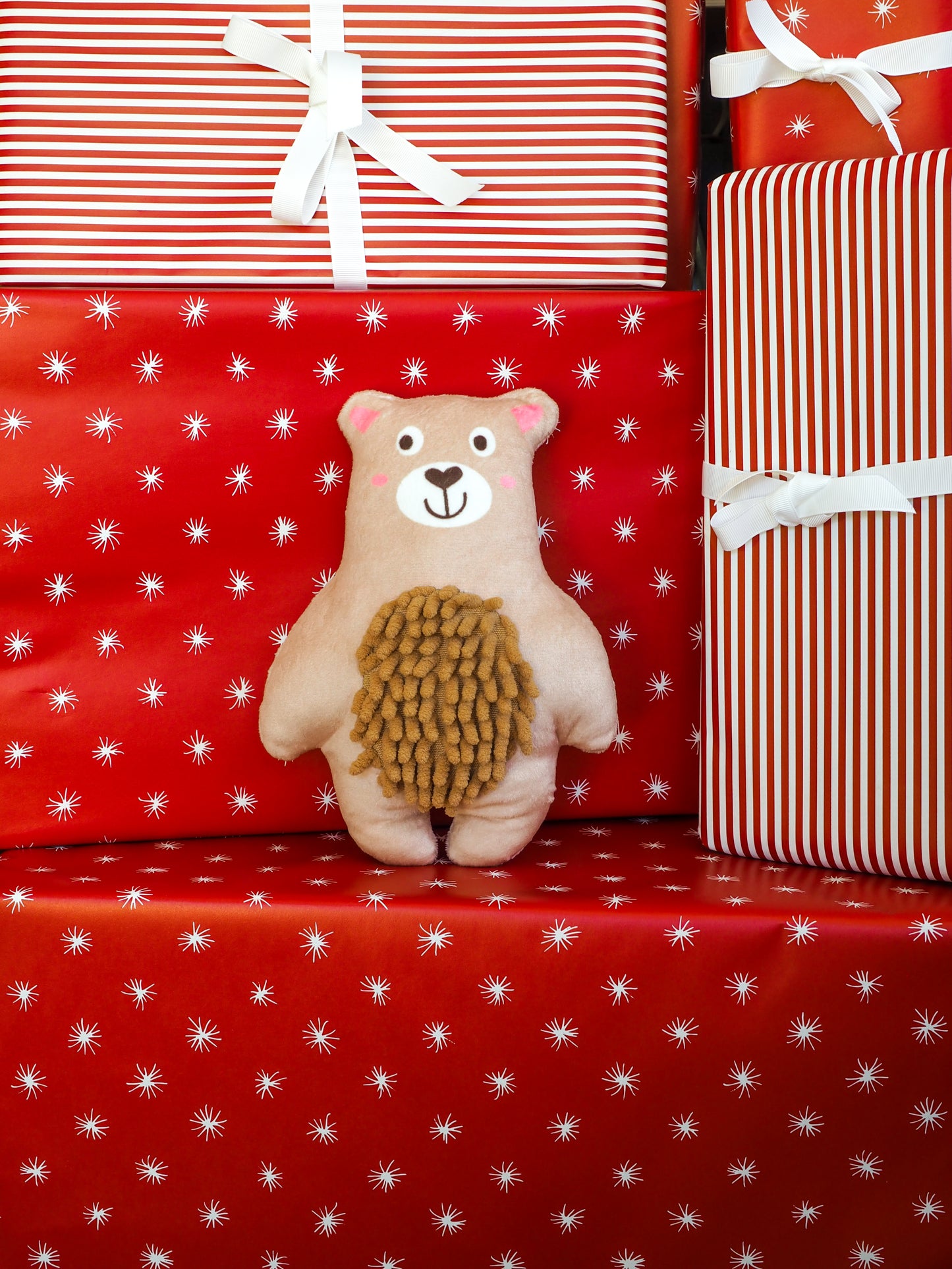 Teddy bear with a hedgehog plush toy on red gift wrap with white star pattern