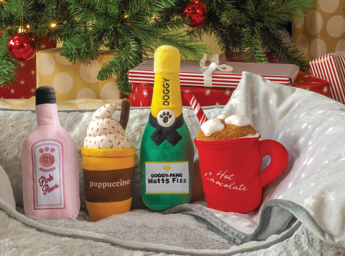 Set of plush drink toys resembling a bottle, ice cream, and hot chocolate mug with Christmas decorations in the background.