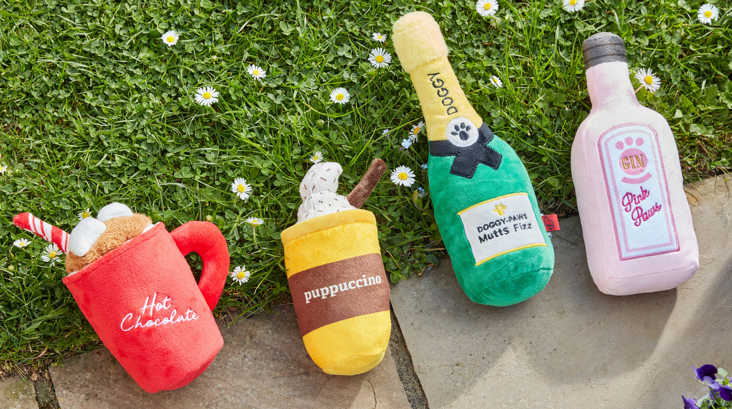 Four colorful plush toys resembling a mug, bottle, and bottles on grass.