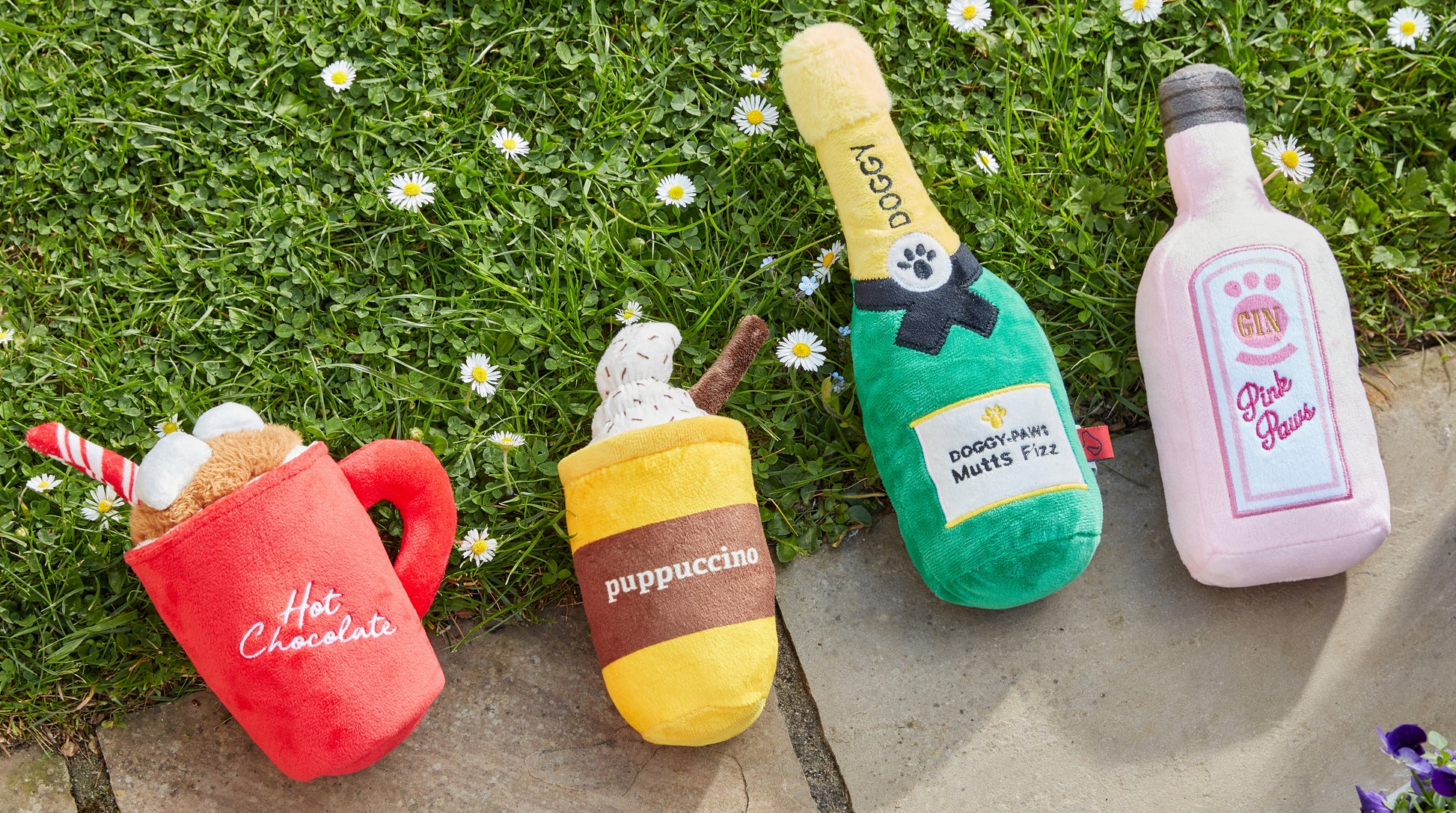 Four colorful plush toys resembling a mug, bottle, and bottles on grass.