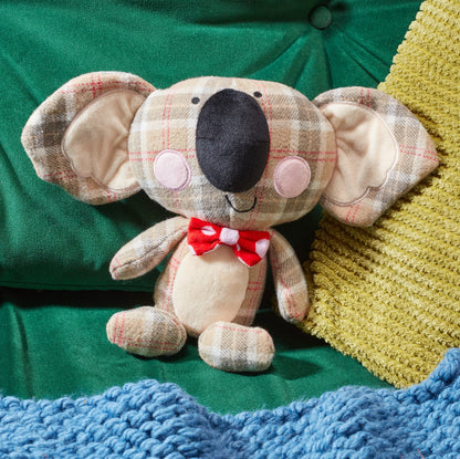 Plush koala toy with a red bow tie on a green fabric background