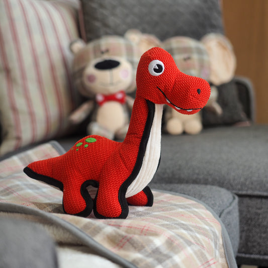 Red dinosaur plush toy on a couch with other plush toys in the background