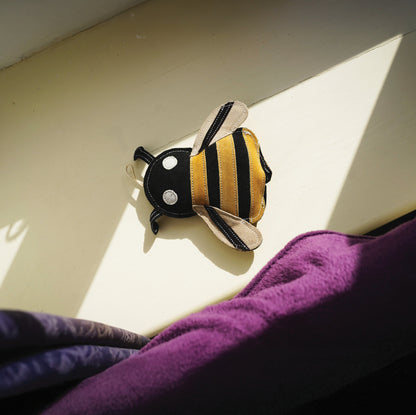 Plush bee toy on a light surface with a purple fabric underneath