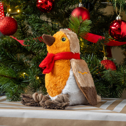 Plush toy penguin with a red scarf in front of a decorated Christmas tree.