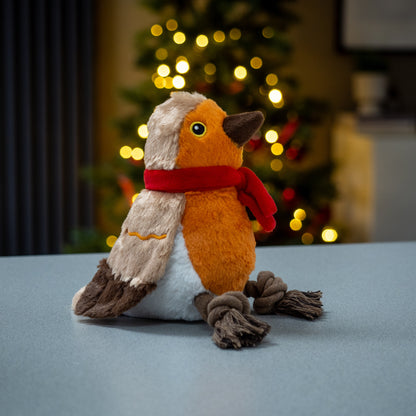 Plush toy resembling a bird with a red scarf in front of a blurred Christmas tree.