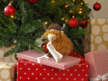 Stuffed animal toy on a red gift box under a decorated Christmas tree with presents.