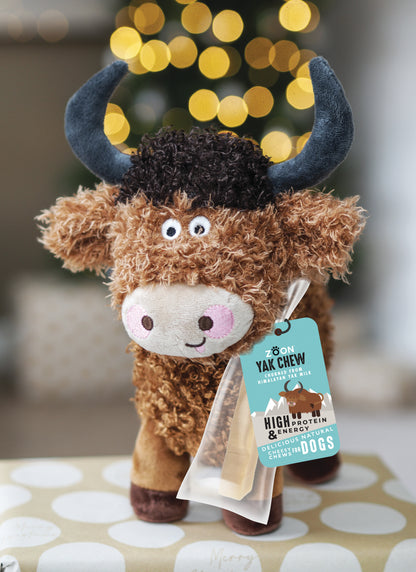 Plush toy yak with a tag on a patterned surface, blurred lights in the background