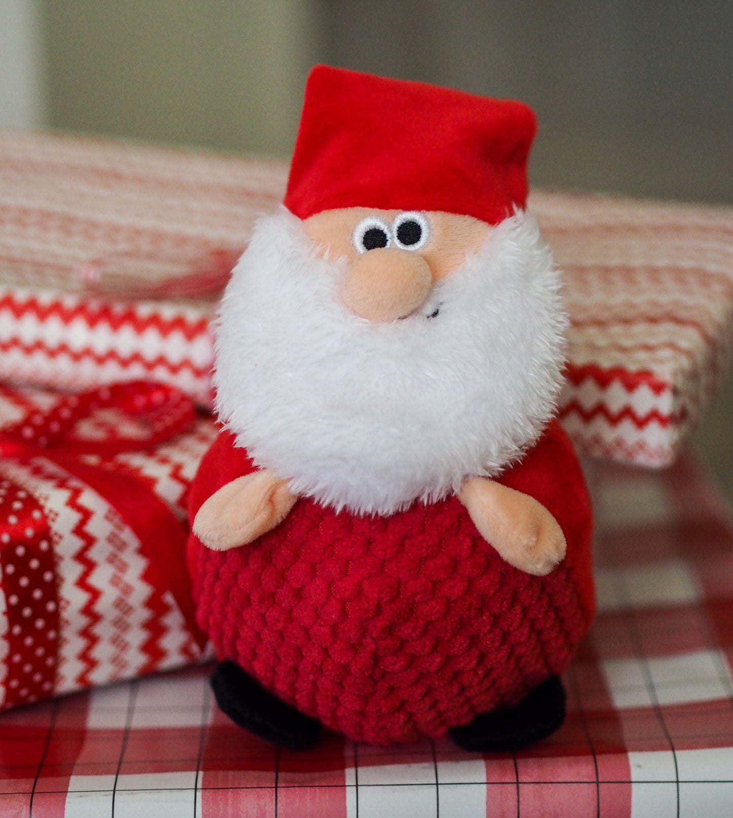 Plush Santa Claus toy on a checkered tablecloth with a blurred background