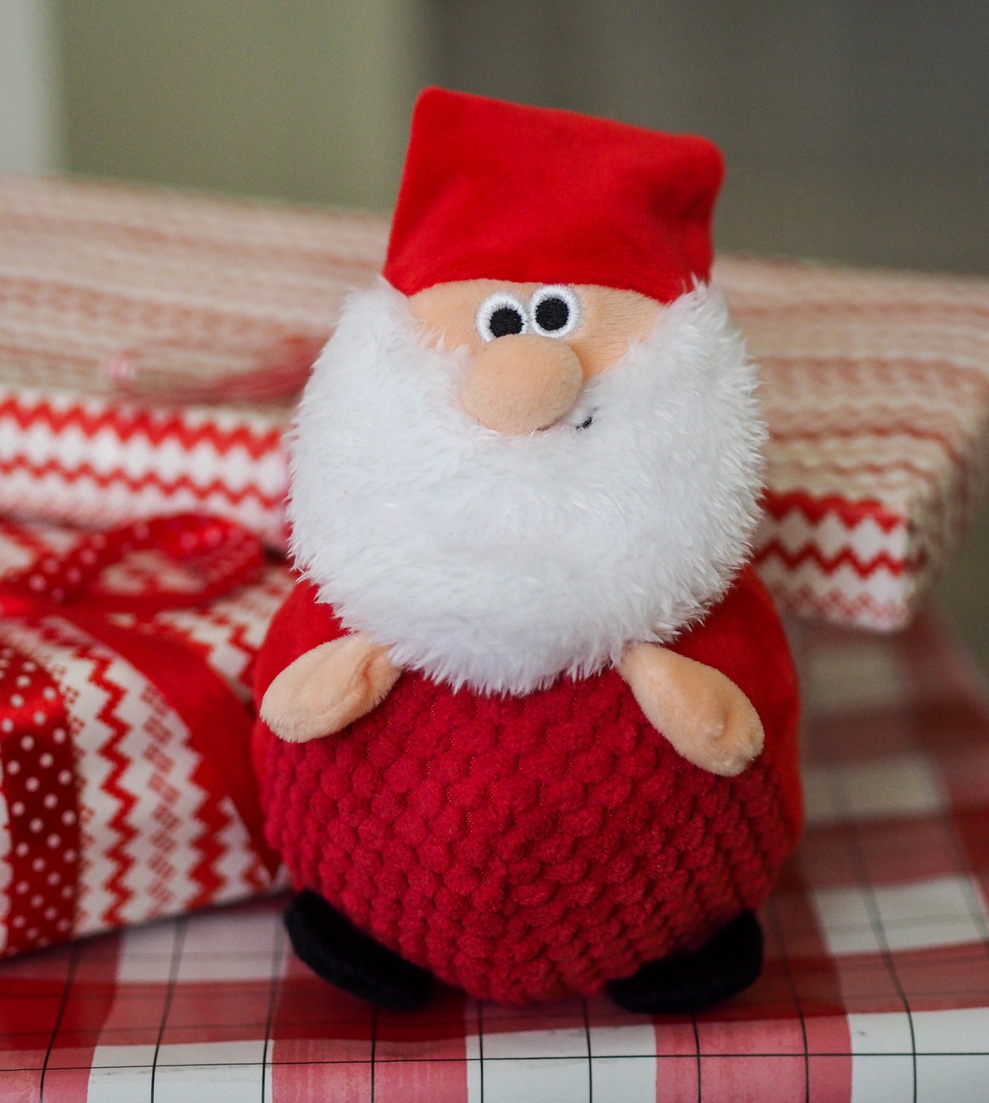 Plush Santa Claus toy on a checkered tablecloth with a blurred background