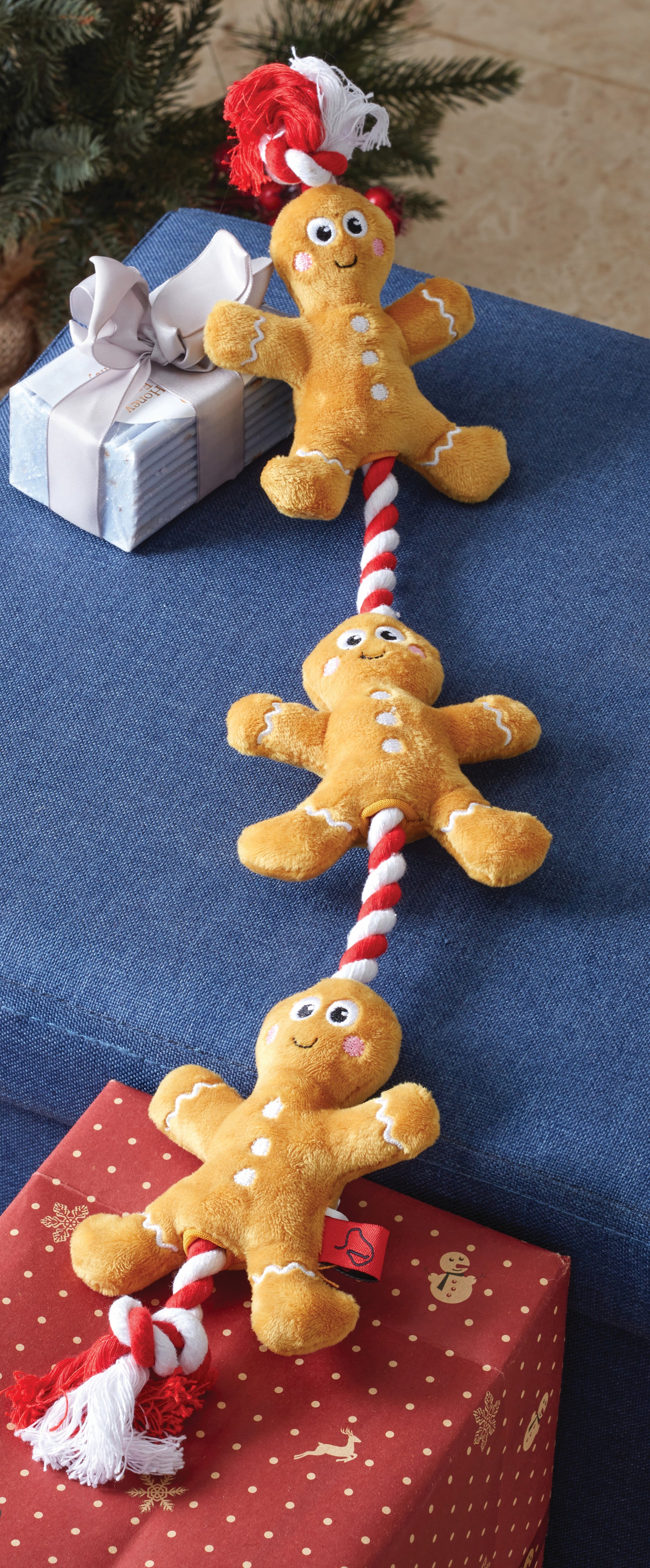 Gingerbread man toy with candy cane on a blue surface with Christmas decorations.