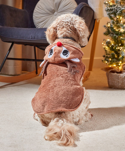 Dog wearing a reindeer costume in a cozy living room setting with a Christmas tree.