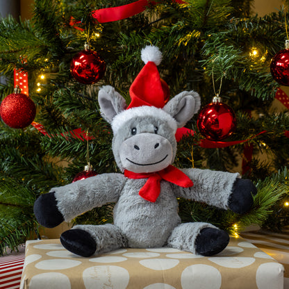 Plush donkey toy wearing a Santa hat and red bow tie in front of a decorated Christmas tree.