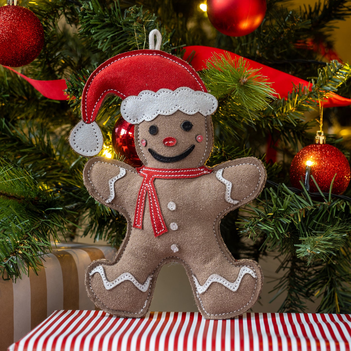 Gingerbread man ornament with a red hat and scarf on a Christmas tree background