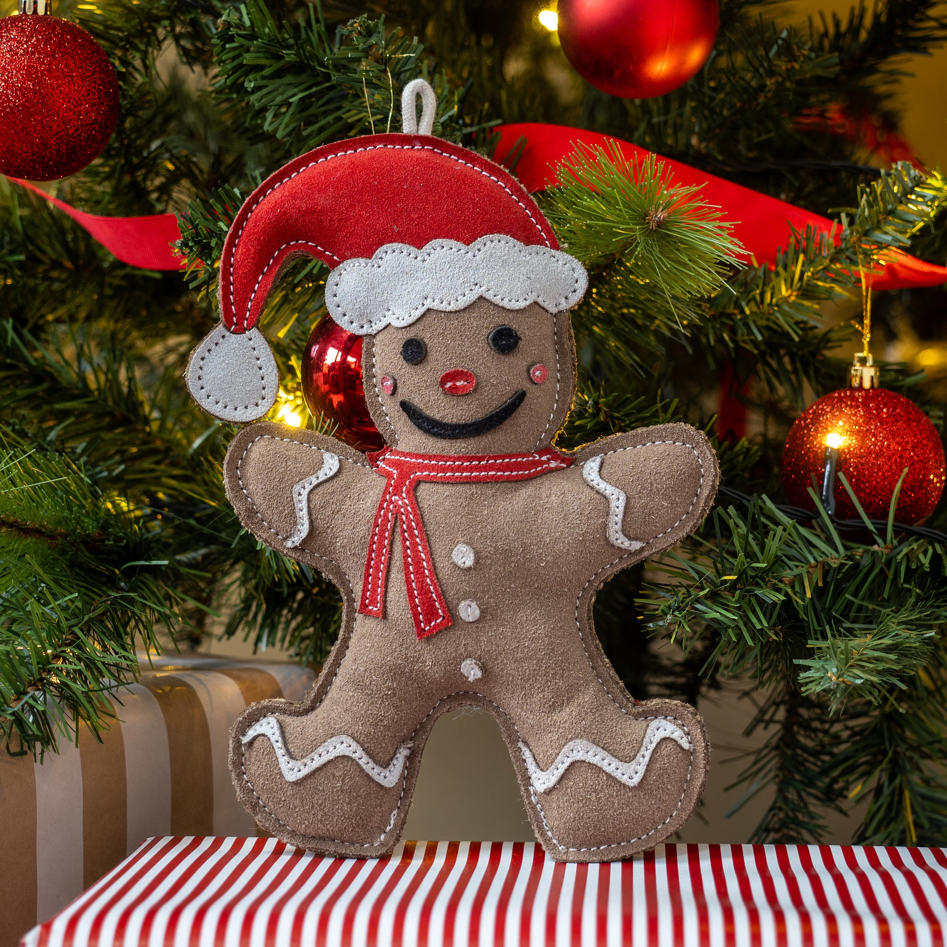 Gingerbread man ornament with a red hat and scarf on a Christmas tree background