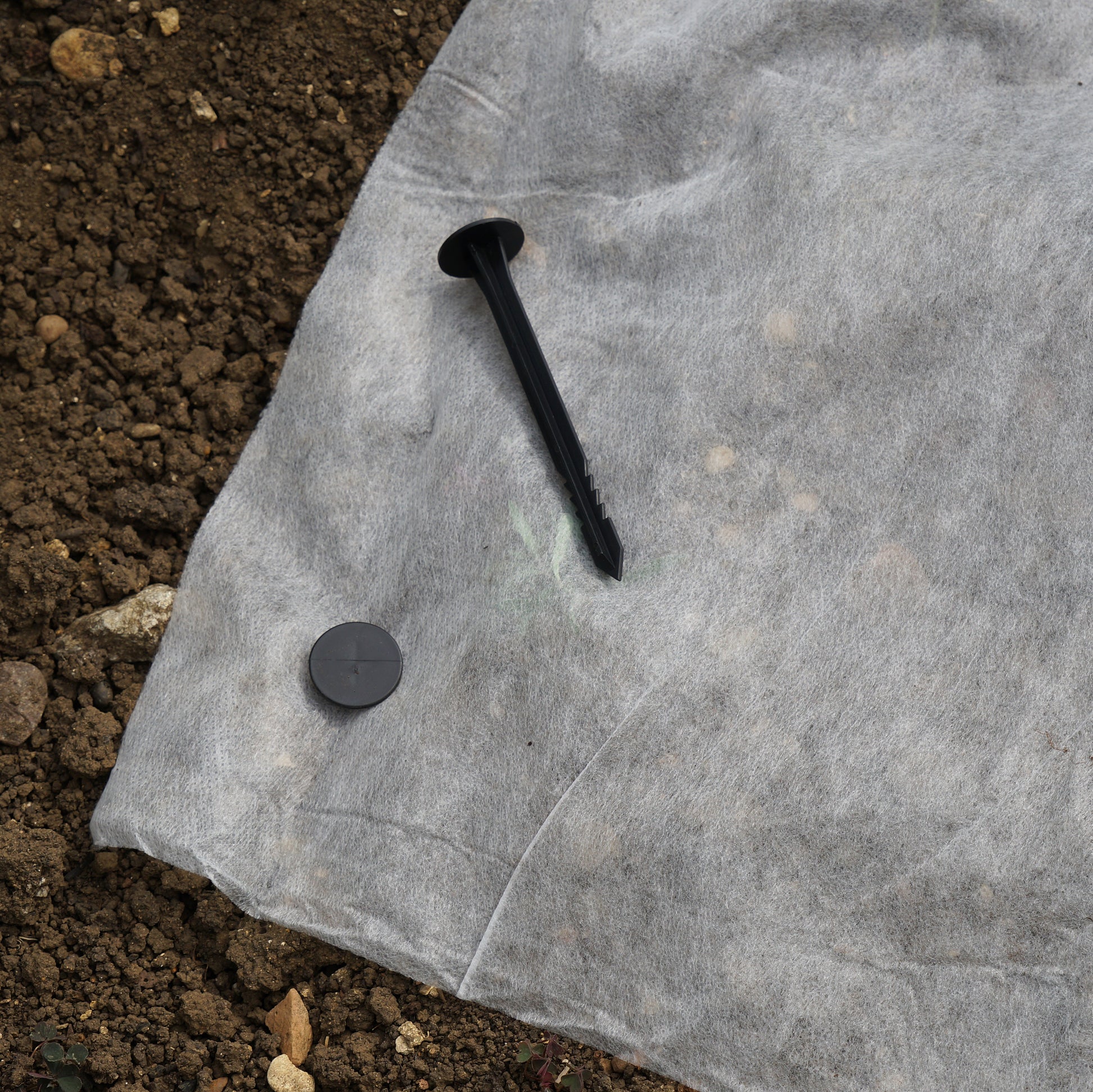 Black nail and washer on a piece of gray fabric with soil in the background