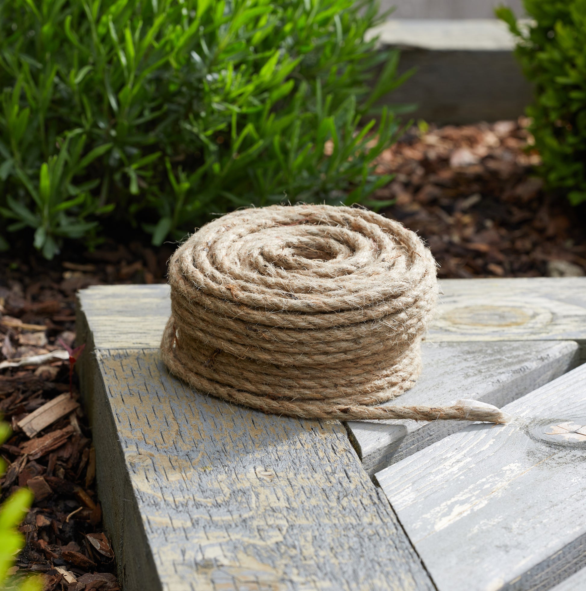 Rolled-up piece of rope on a wooden surface with greenery in the background