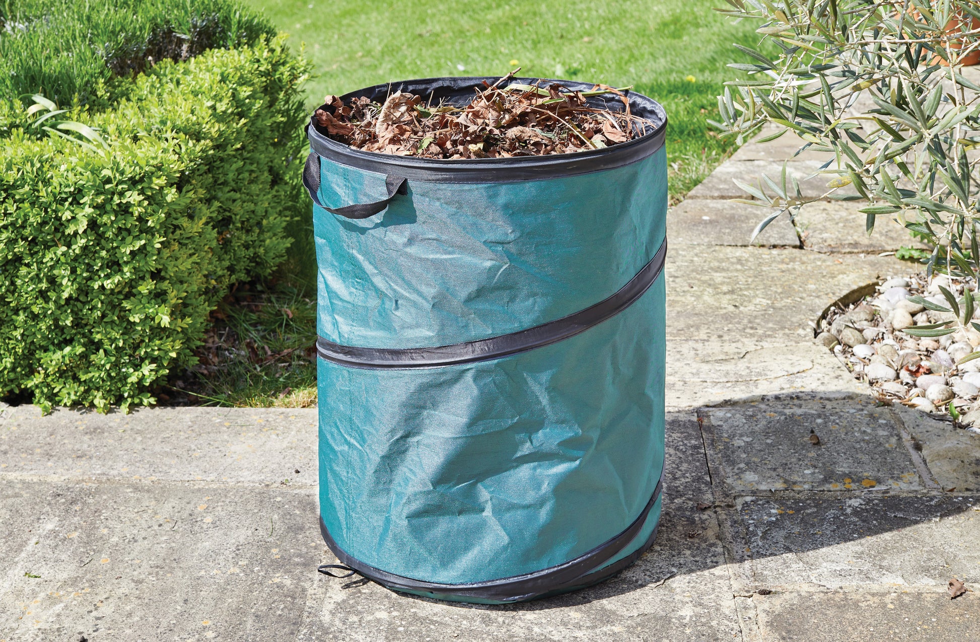 Green garden waste bin on a slab path with plants around