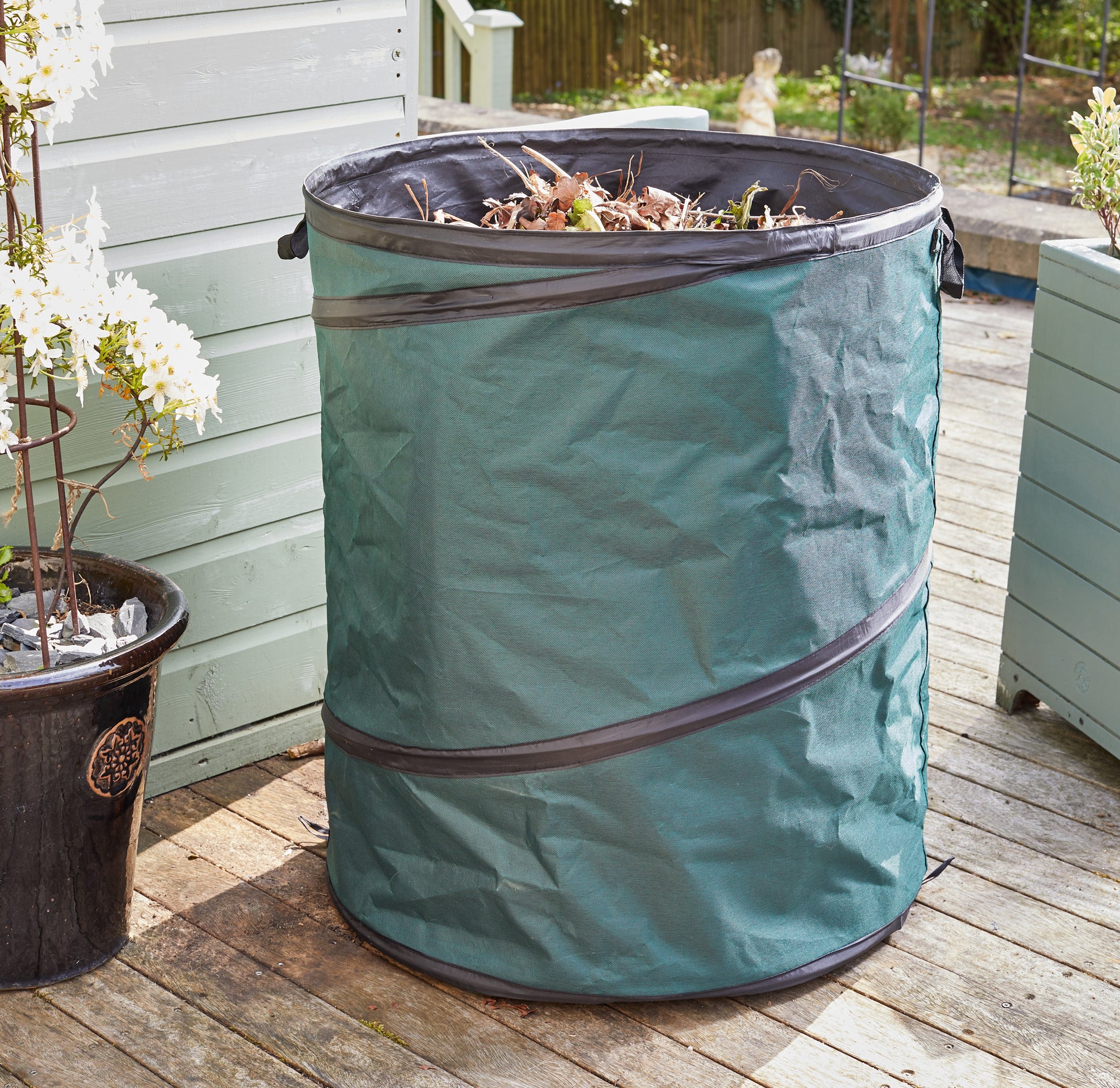 Green garden waste bin on a wooden deck with plants around