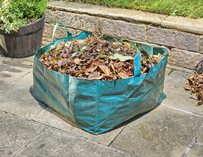 Green garden waste bag filled with leaves on a stone patio