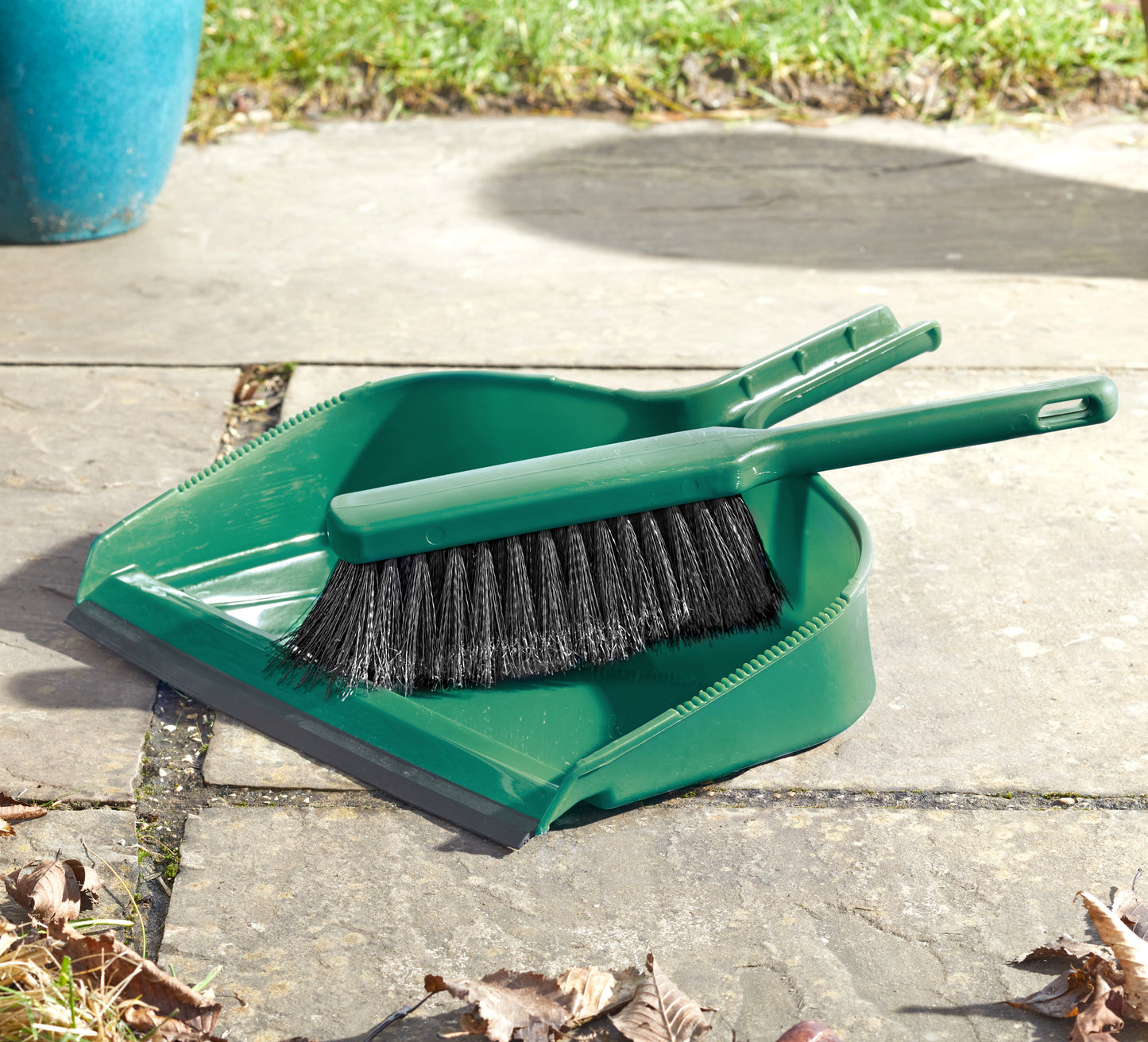 Green dustpan and brush set on a concrete surface with leaves around