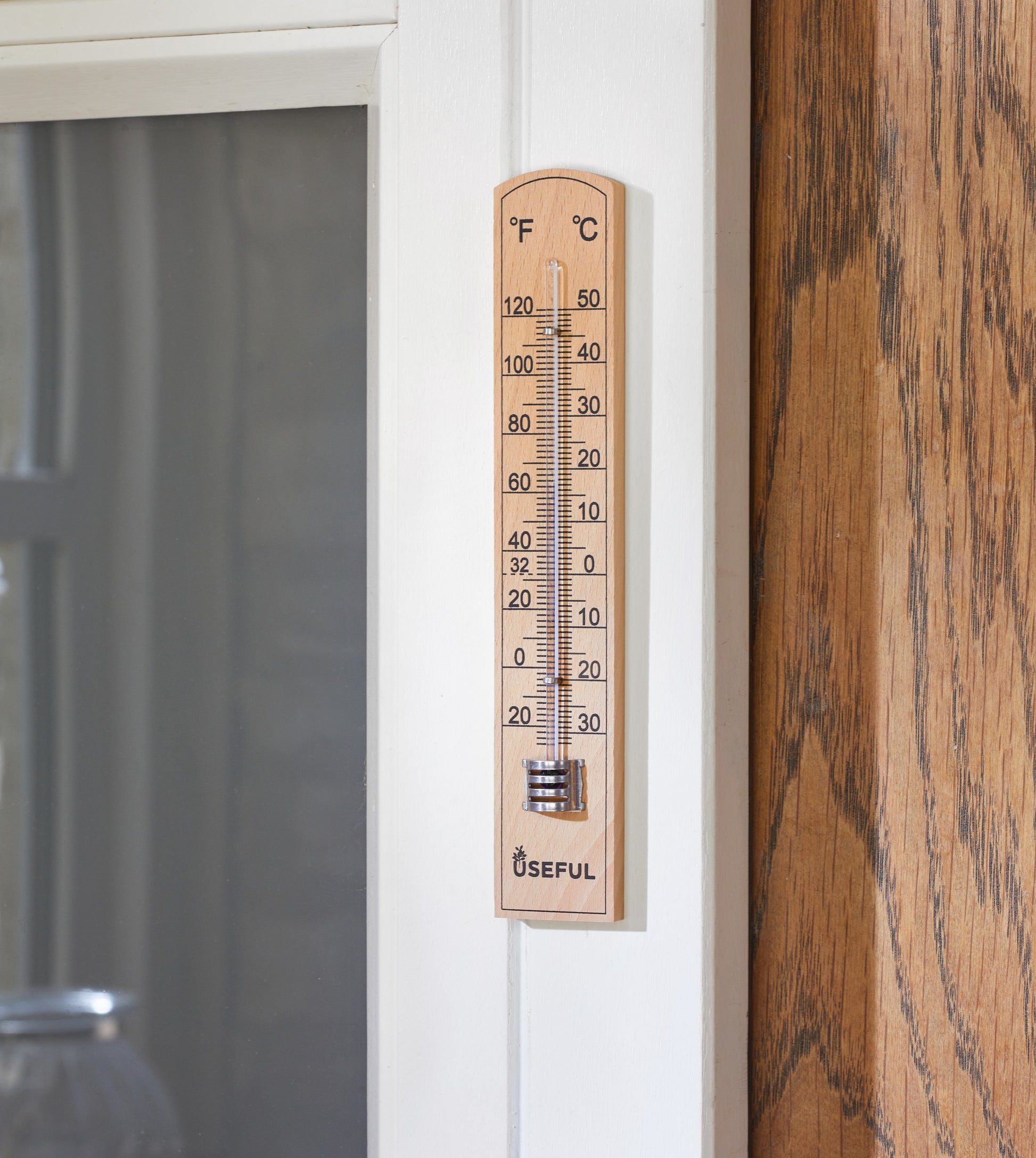 Wooden thermometer attached to a door with a wooden surface and glass panel in the background.