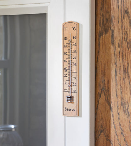 Wooden thermometer attached to a door with a wooden surface and glass panel in the background.