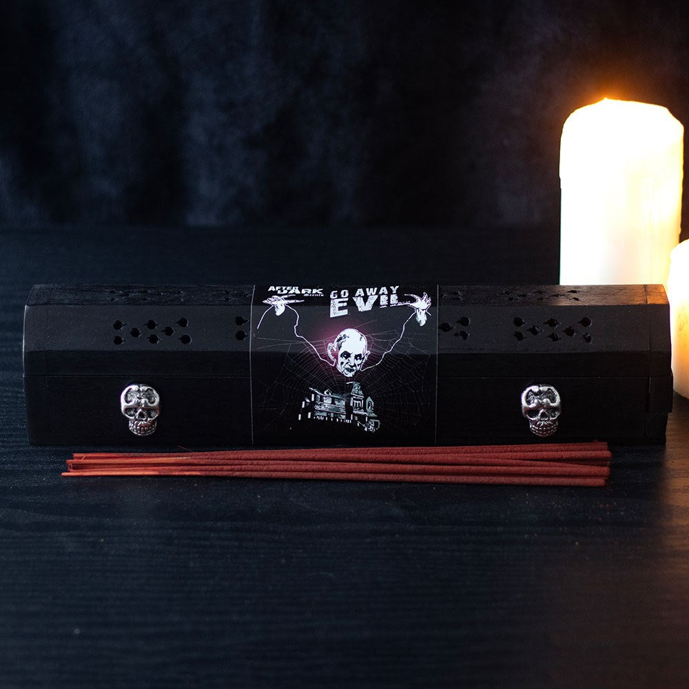 Black incense burner with skull designs on a dark background with candles.