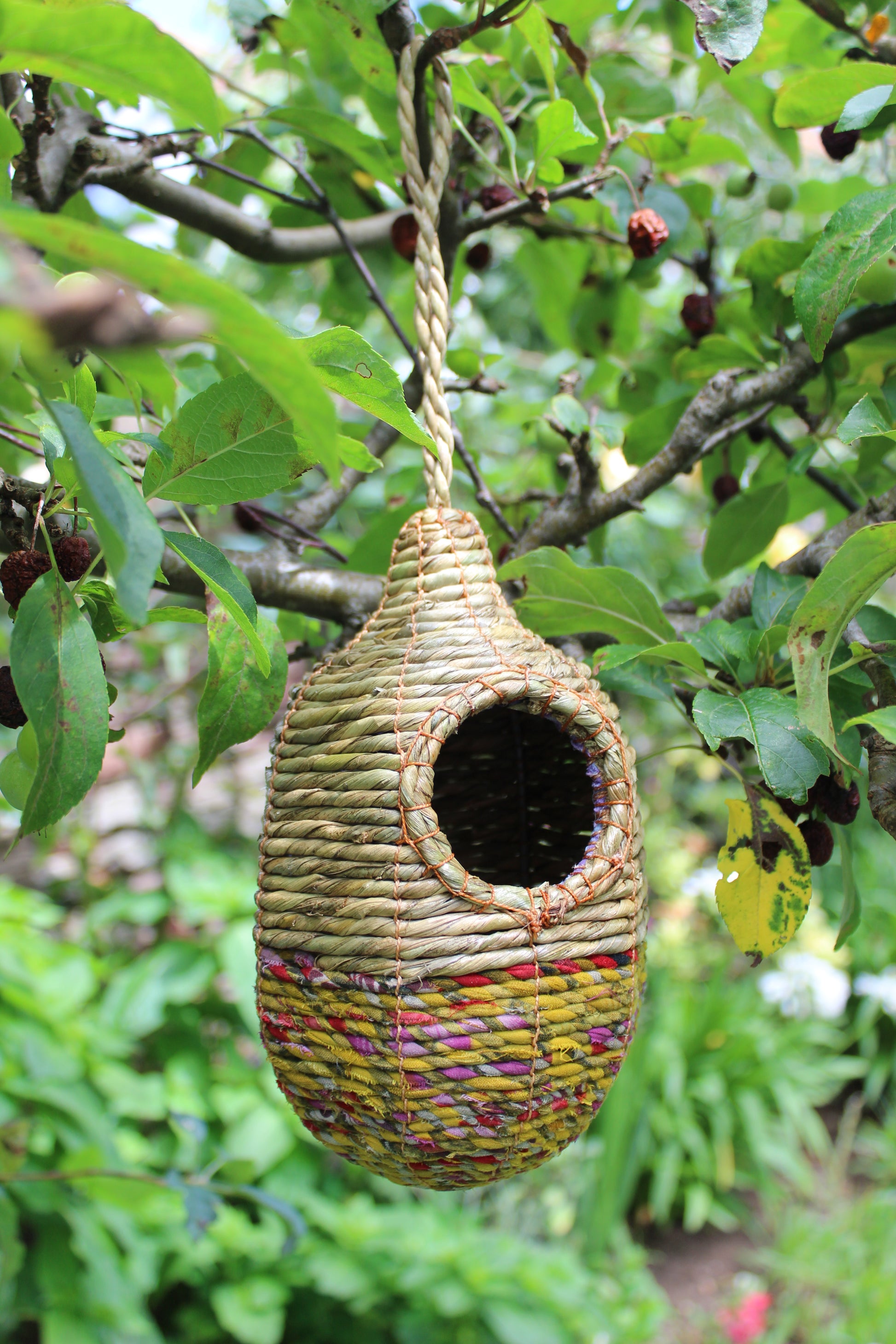 Handmade birdhouse with colorful woven design hanging in a tree
