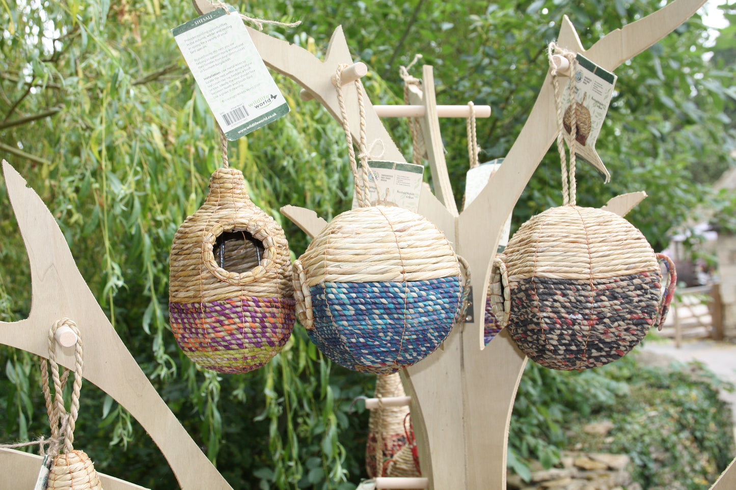 Woven birdhouses hanging from a wooden structure with greenery in the background