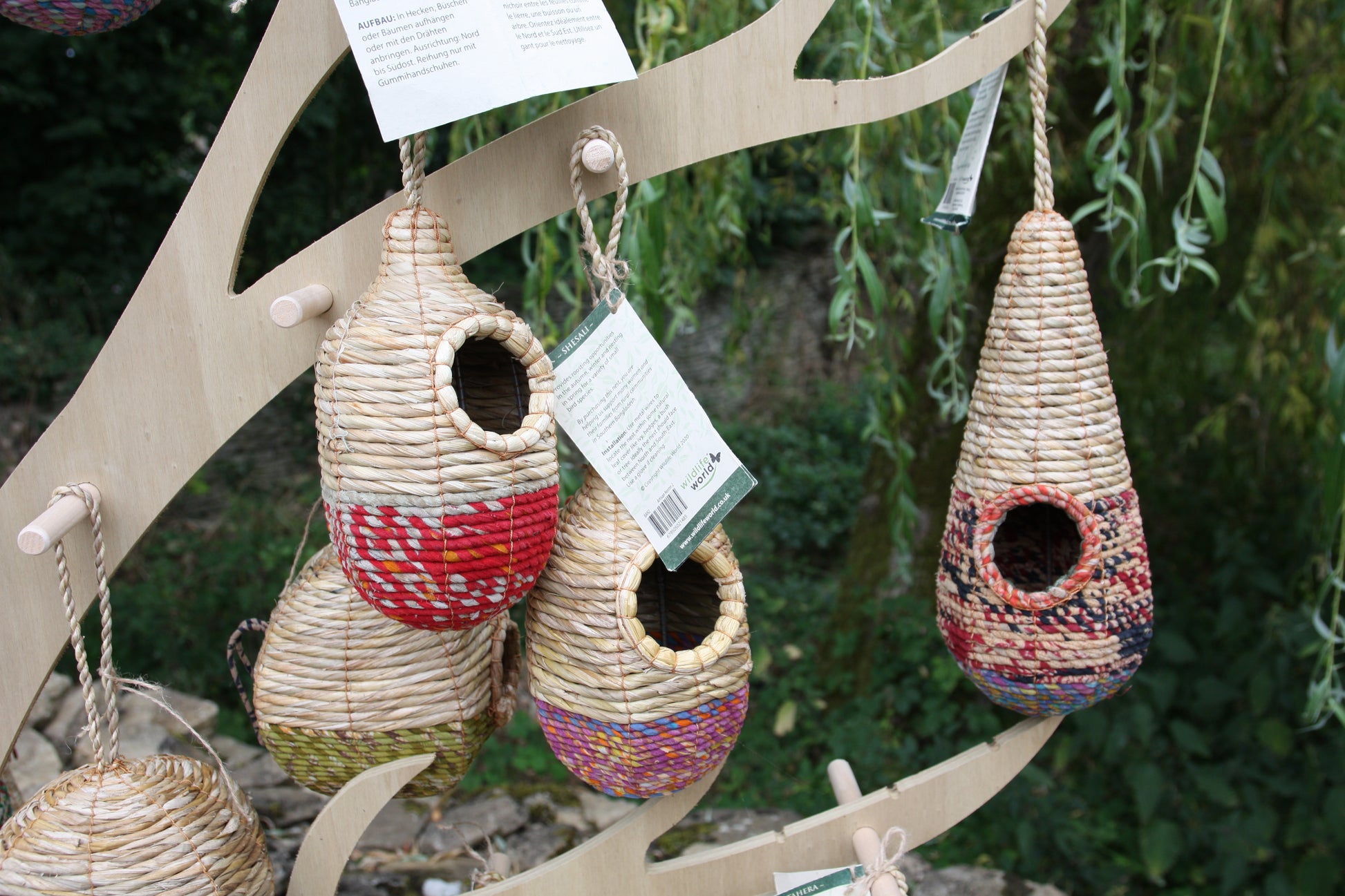 Woven birdhouses hanging from a branch with greenery in the background