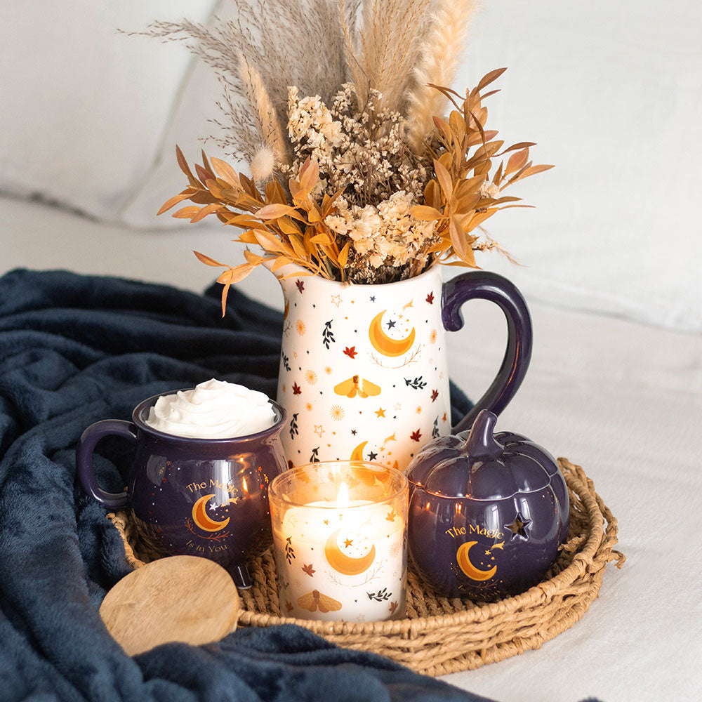 Decorative setting with mugs, a candle, and a vase with dried flowers on a tray.