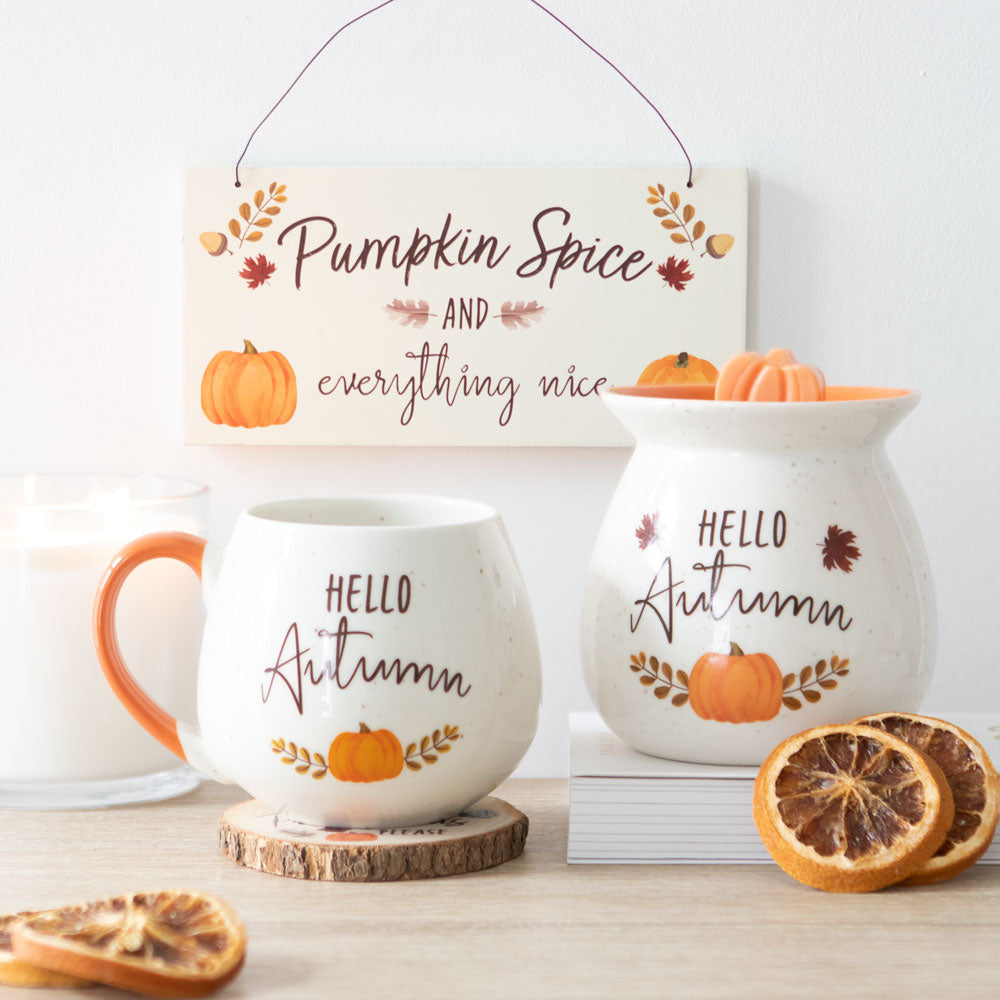 Autumn-themed decor items including a mug, sign, and candle on a wooden surface.