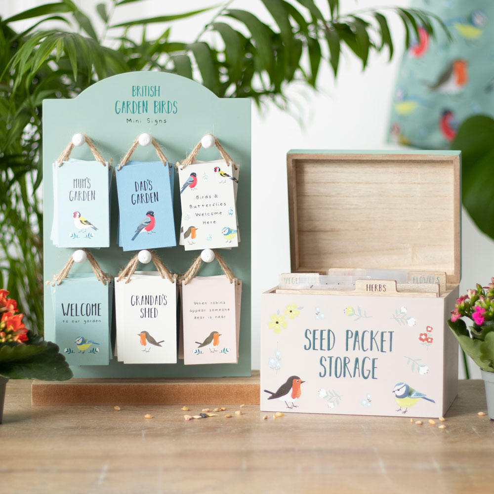 Decorative seed packet display with a wooden storage box on a table with plants in the background.