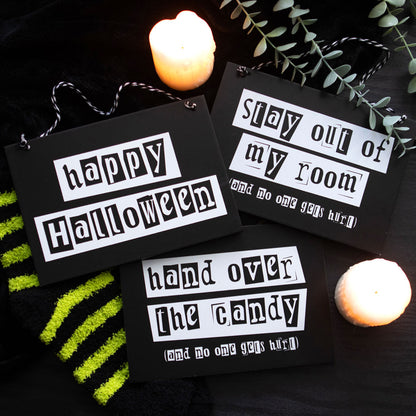 Halloween-themed signs with text on a dark background with candles and greenery.