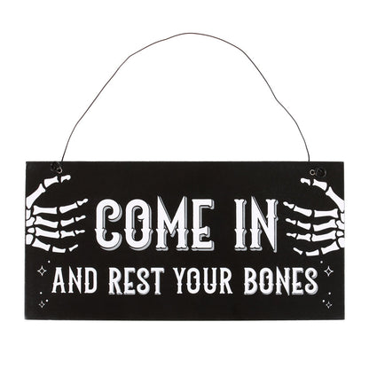 Hanging sign with skeleton hands and text 'Come in and rest your bones' on a black background