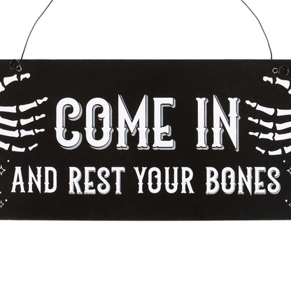 Decorative sign with skeleton hands and text 'COME IN AND REST YOUR BONES' on a black background.