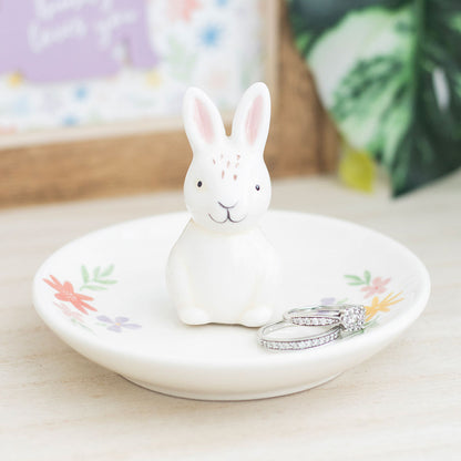 White ceramic rabbit on a decorative plate with floral designs, placed on a light surface.