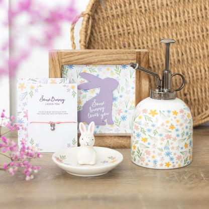 Decorative items including a soap dispenser, rabbit figurine, and cards on a wooden surface with floral decorations.