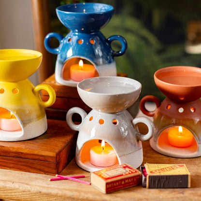 Four ceramic oil burners with lit candles on a wooden surface, surrounded by matches.