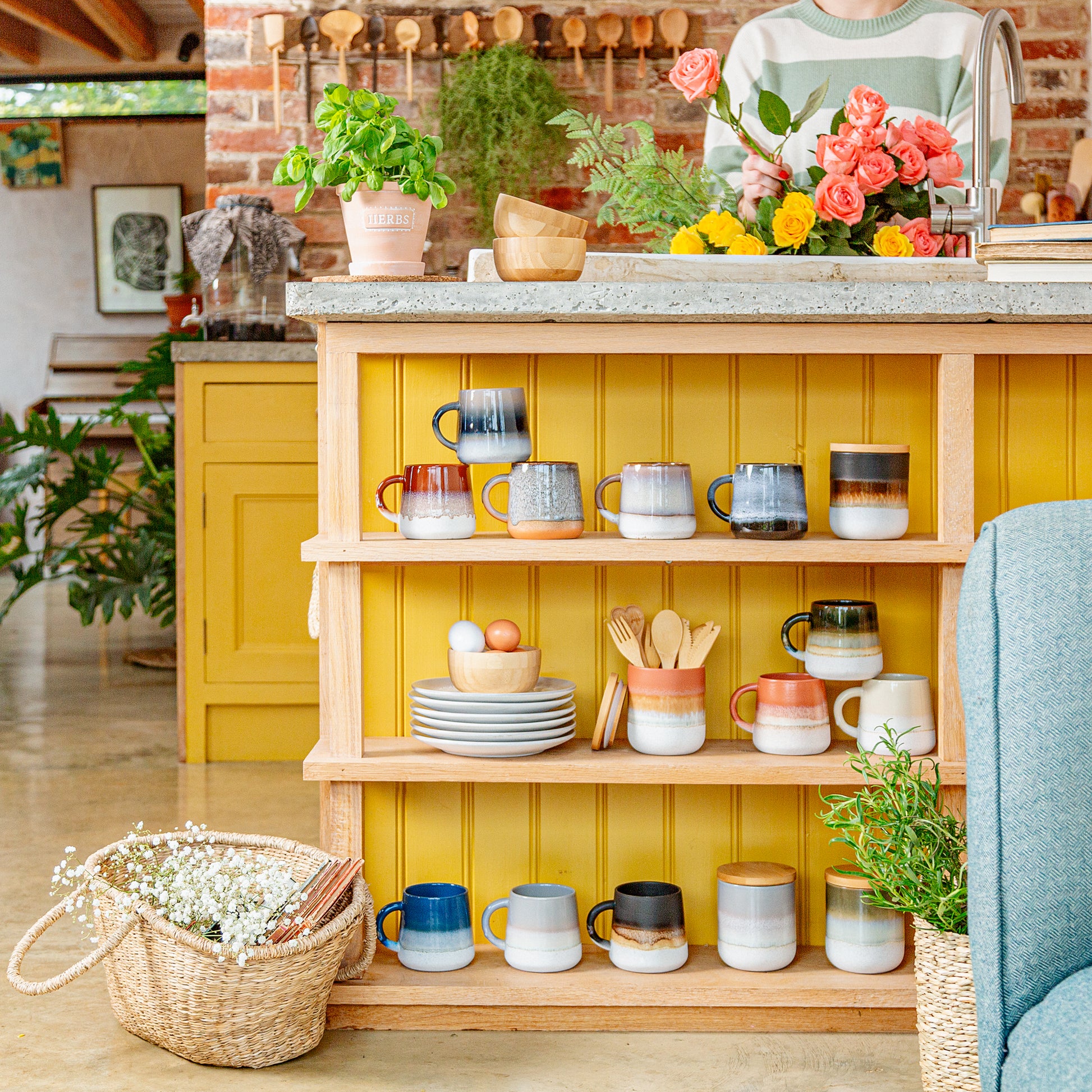 Kitchen island with ceramic mugs, plates, and utensils against a yellow wall.