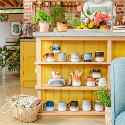 Kitchen island with ceramic mugs, plates, and utensils against a yellow wall.