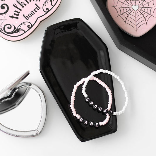 Black coffin-shaped jewelry box with 'Spooky Babe' beaded bracelets on a white surface.