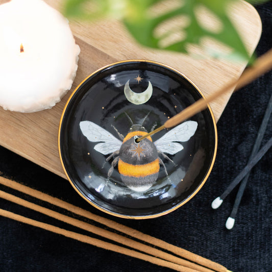 Black dish with bee design on a wooden surface with candles and incense sticks.