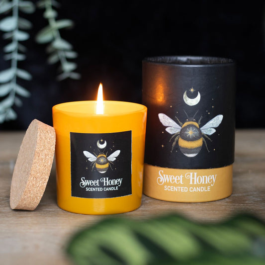 Yellow scented candle with 'Sweet Honey' label and black container with bee design on a wooden surface.