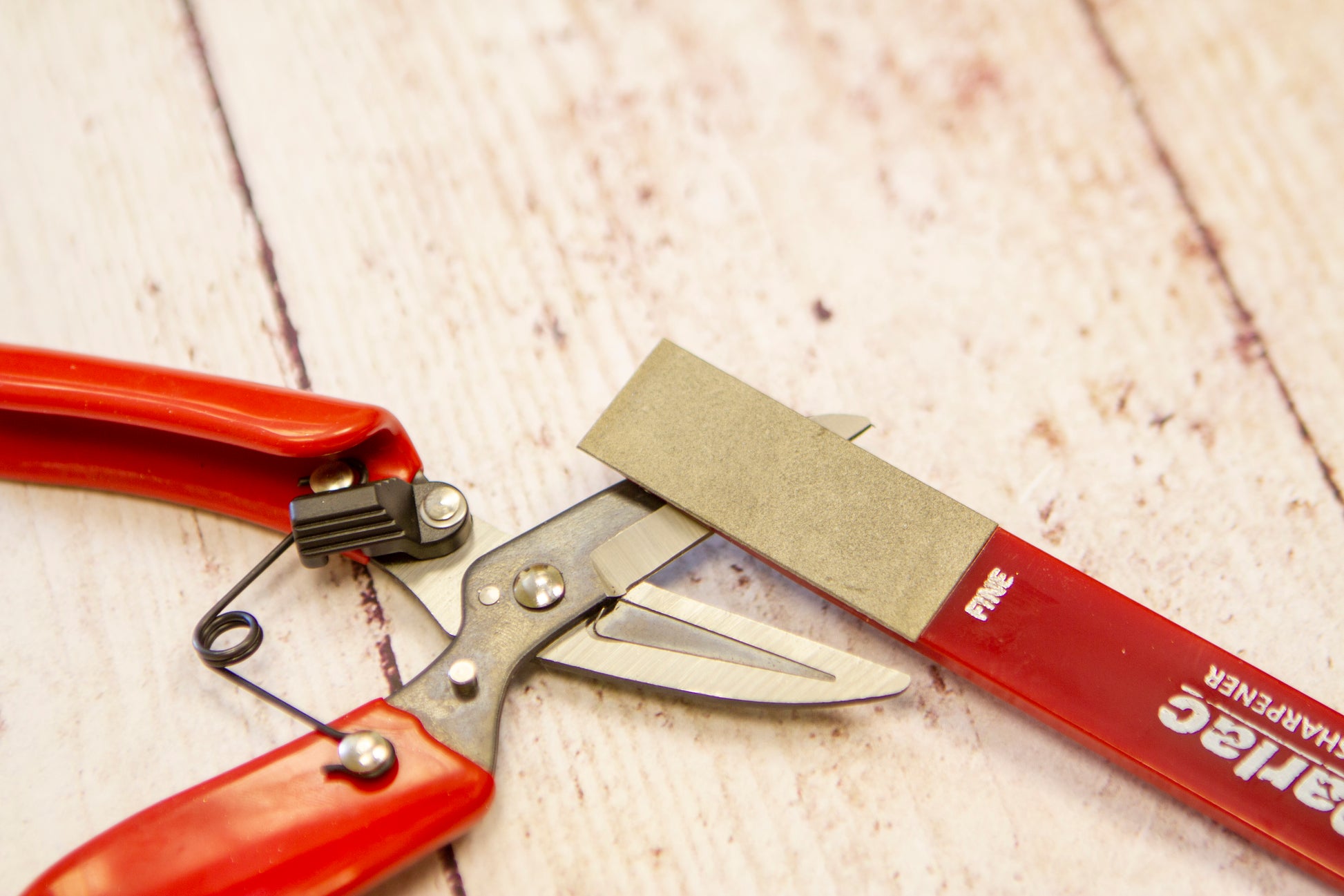 Red-handled pruning shears with a sandpaper block on a wooden surface