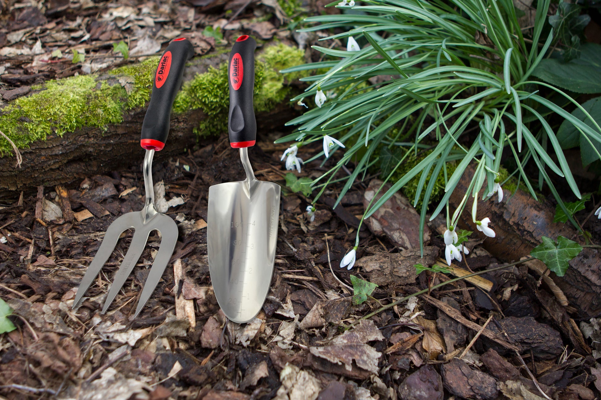 Gardening tools including a trowel and fork on a garden bed with plants and flowers.