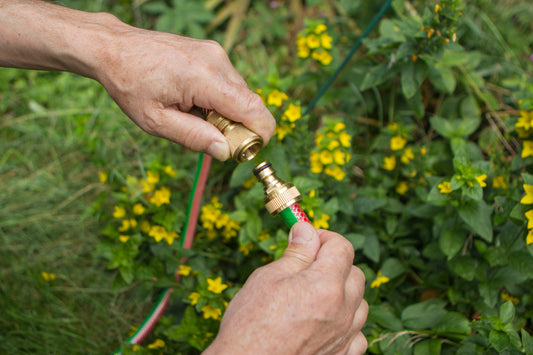 Person connecting two garden hoses with a background of greenery and yellow flowers