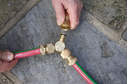 Hand connecting a garden hose to a brass fitting on a stone pavement.