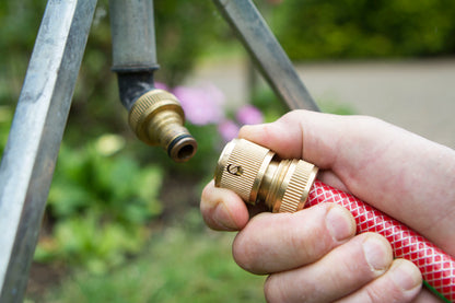 Hand connecting a red garden hose to a brass fitting outdoors.